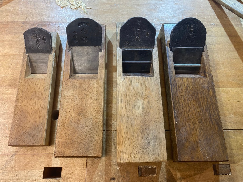 Four Japanese kanna planes arranged left to right from rough to fine, showing blade curvature differences and absence of chipbreakers on coarse planes